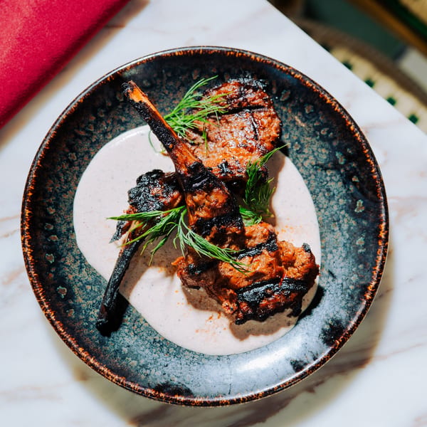 Three grilled lamb chops with a creamy sauce and fresh dill on a dark, speckled plate.