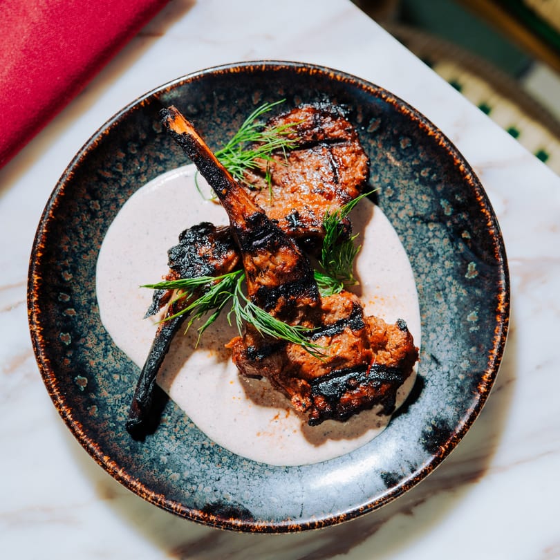 Three grilled lamb chops with a creamy sauce and fresh dill on a dark, speckled plate.