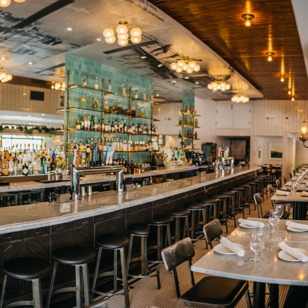 A long, well-stocked bar with stools and dining tables set for guests in a restaurant.
