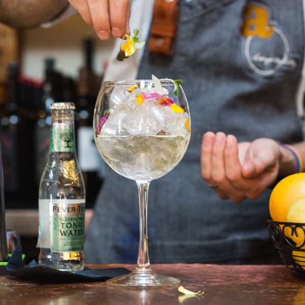 Bartender garnishing a large gin and tonic with edible flowers at AMBAR.