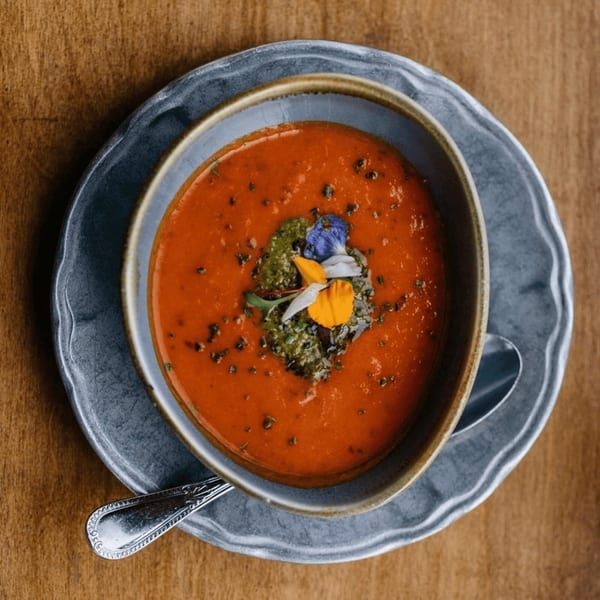Overhead view of a bowl of red tomato soup with green pesto and edible flowers.