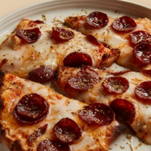 Close-up of several slices of pepperoni pizza on a white plate, topped with herbs.