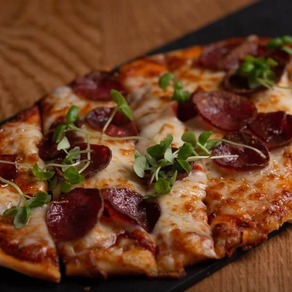 Pepperoni flatbread pizza with melted cheese and fresh green garnish on a dark serving board.