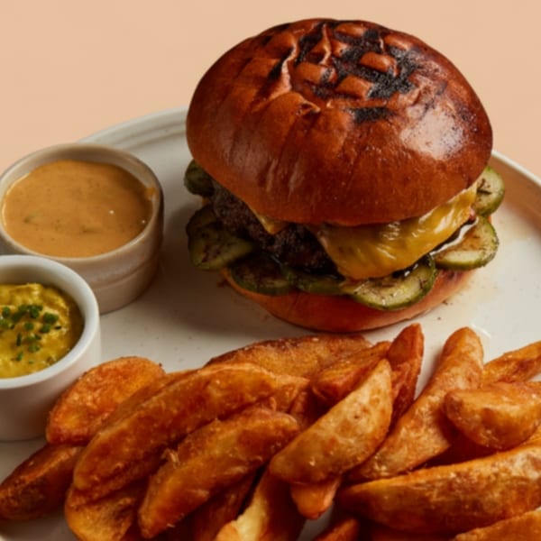 AMBAR's European burger with cheese and pickles, served with potato wedges and two dipping sauces.