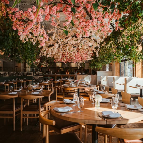 Restaurant dining room with wooden tables and chairs, adorned with pink and white cherry blossoms overhead.
