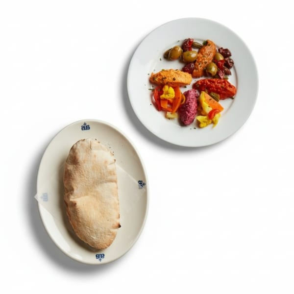A plate of colorful European dips and olives next to a plate with pita bread.