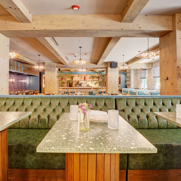 Restaurant interior with green leather booths, speckled tables, and an open kitchen in the background.