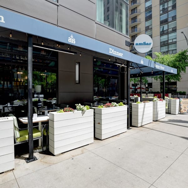 Ambar restaurant's outdoor patio with blue awnings, white planters, and dining tables on a sunny day.
