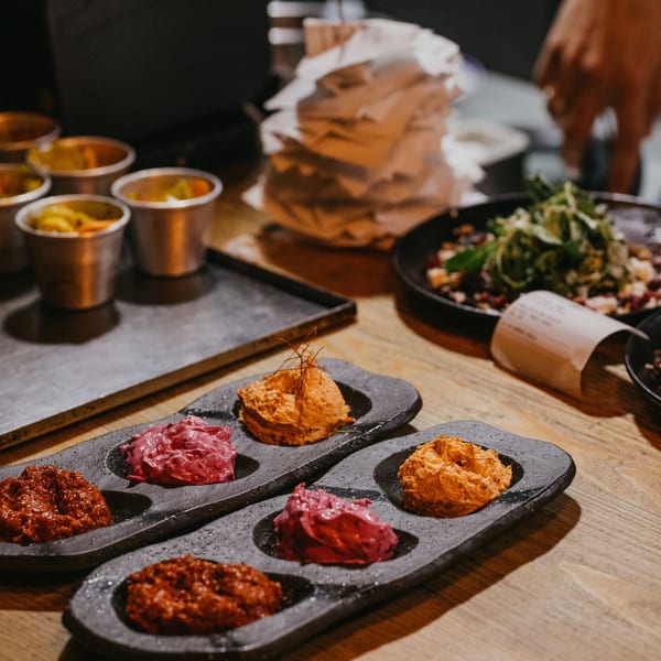 Two black serving dishes with colorful European spreads, alongside small metal cups of pickled vegetables.