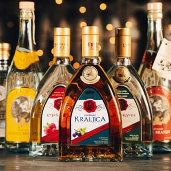 A collection of European brandy bottles, including "Kraljica" in the foreground, with warm bokeh lights.