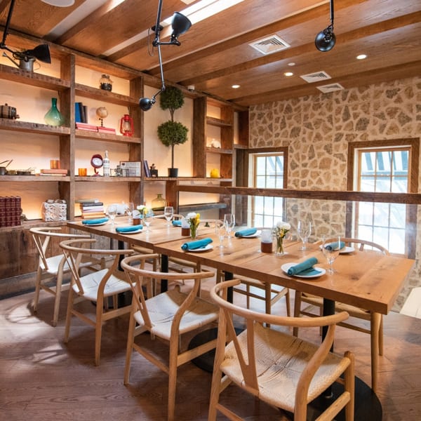 A long wooden dining table set for guests, surrounded by wooden chairs in a rustic restaurant.