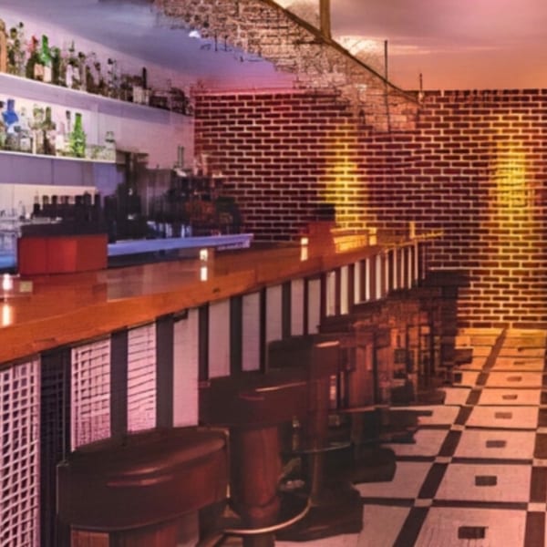 A dimly lit bar with a long wooden counter, bar stools, and shelves of bottles against a brick wall.