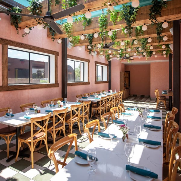 A long, empty dining room with pink walls, checkered floors, and tables set with teal napkins.