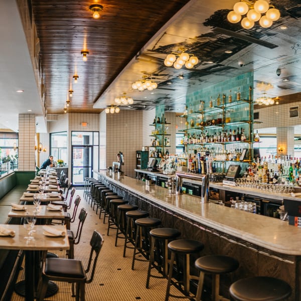 A long, narrow restaurant interior with a full bar, dining tables, and warm lighting.