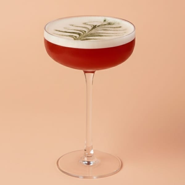A vibrant red cocktail with a delicate white foam and green leaf design in a coupe glass.