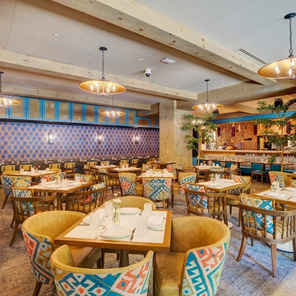 Spacious restaurant dining room with patterned chairs, wooden tables, and blue and gold decor.
