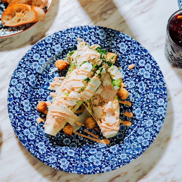 Caesar salad with shaved parmesan, croutons, and dressing on a blue and white patterned plate.
