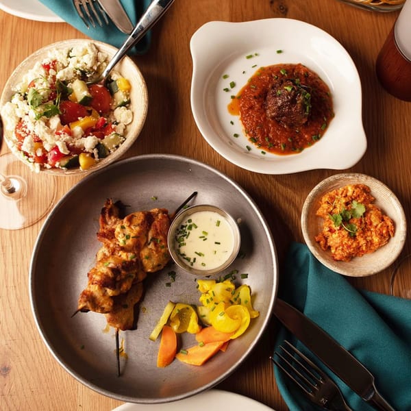 Overhead view of various European dishes including skewers, salad, and meatballs on a wooden table.