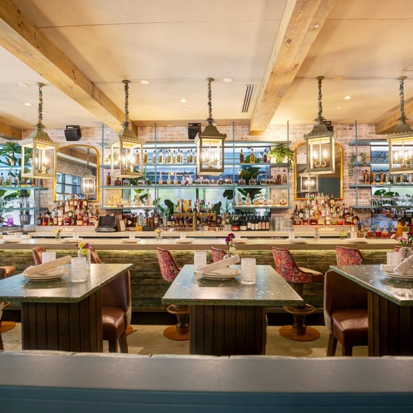 A restaurant bar with bottles on shelves, hanging lanterns, and tables with place settings.