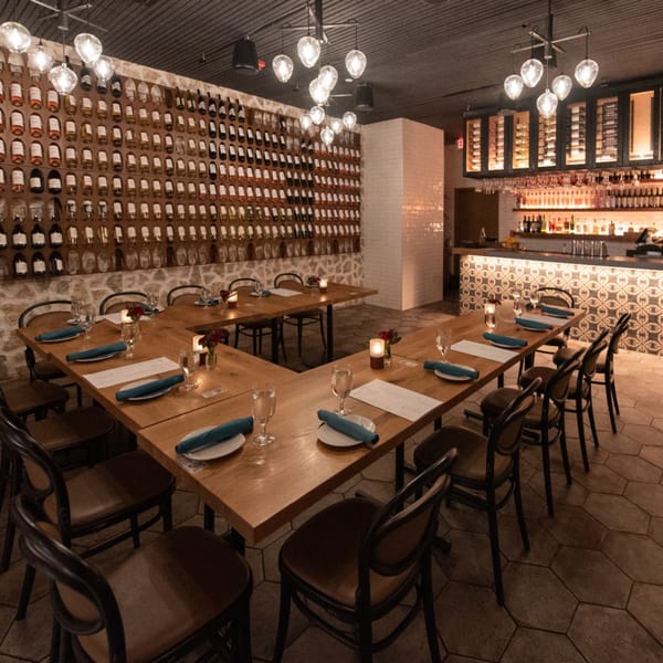 U-shaped dining table set with blue napkins, wine bottle wall, and a patterned bar in a restaurant.