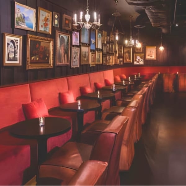 A dimly lit restaurant interior with red velvet booth seating, dark tables, and framed artwork on the walls.