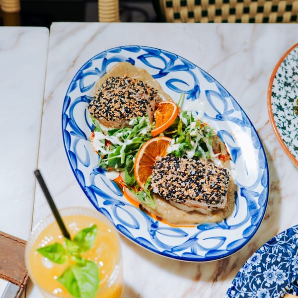 Sesame-crusted fish with arugula, orange slices, and sauce on a blue and white patterned plate.