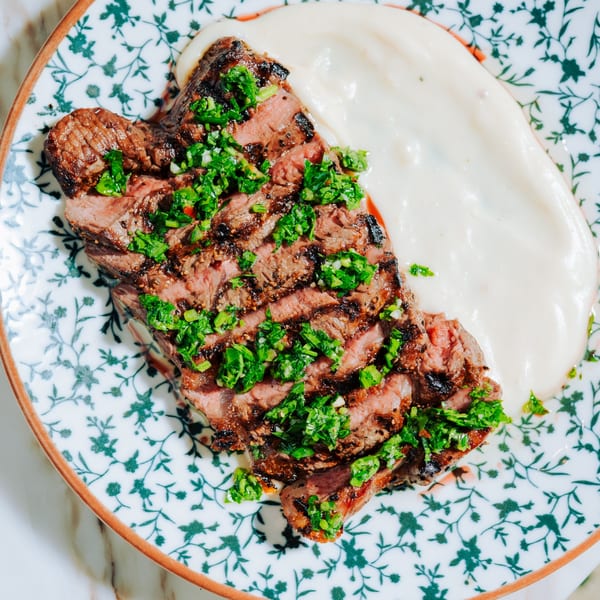 Grilled steak with chimichurri sauce and a side of creamy white puree on a patterned plate.