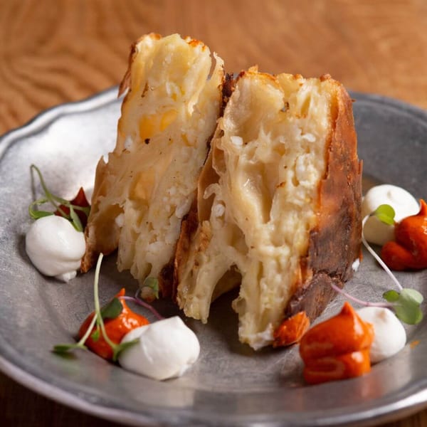 Two pieces of European baked pasta with cheese, garnished with white and orange sauces and microgreens.