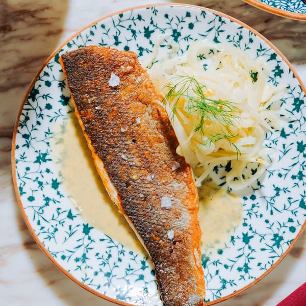 Crispy-skinned fish fillet with fennel salad and sauce on a patterned plate.