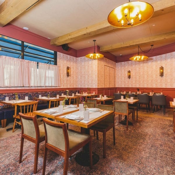 A restaurant dining room with set tables, patterned wallpaper, red wainscoting, and warm lighting.