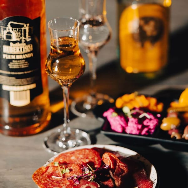 Plum brandy in a glass and bottle, with a plate of cured meats and pickled vegetables.