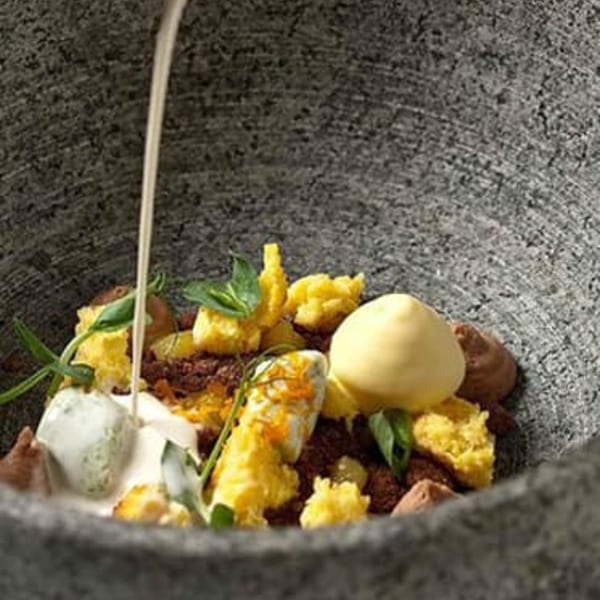 European dessert with yellow cake, chocolate crumbles, ice cream, and sauce being poured.